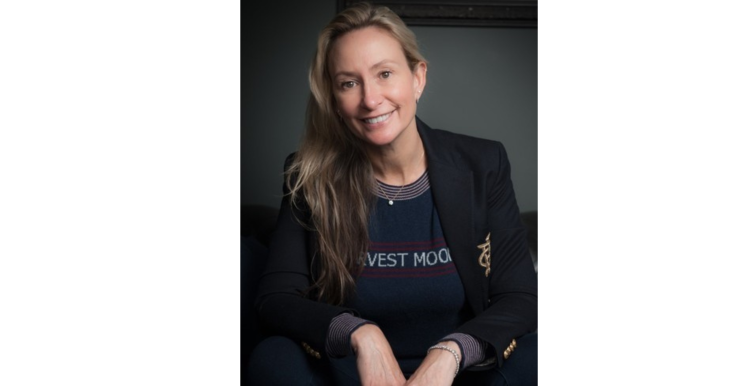 Hicky is wearing a black blazer, with her hair down and is sat smiling at the camera