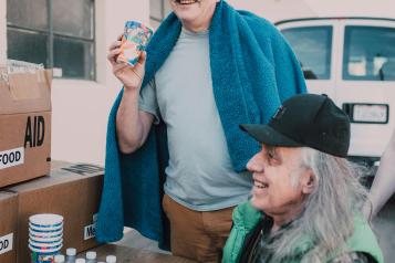 One adult in a wheelchair and one adult holding a cup waiting for food at a food bank.