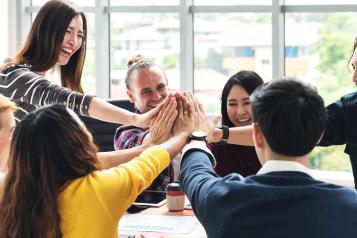 group of people around a table all putting their hands in the middle to high five each other