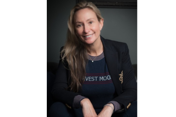Hicky is wearing a black blazer, with her hair down and is sat smiling at the camera