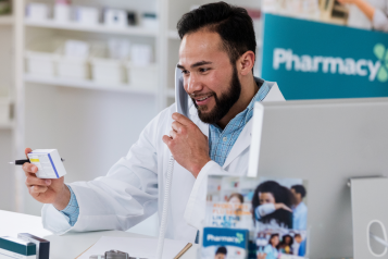 Pharmacist behind the counter, on the phone and holding a medicine box looking at it and smiling