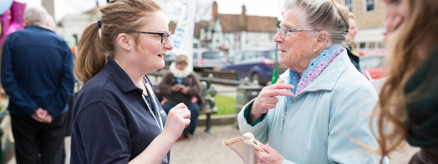 A female volunteer talking to an elderly lady at a community event. 