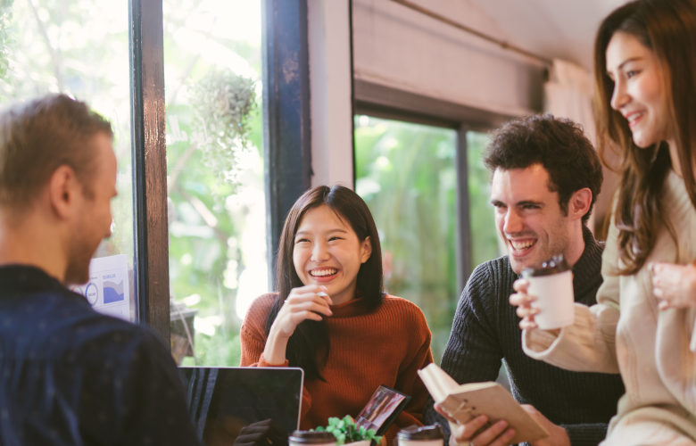People gathered together on a table, with laptops and coffee, having a discussion.