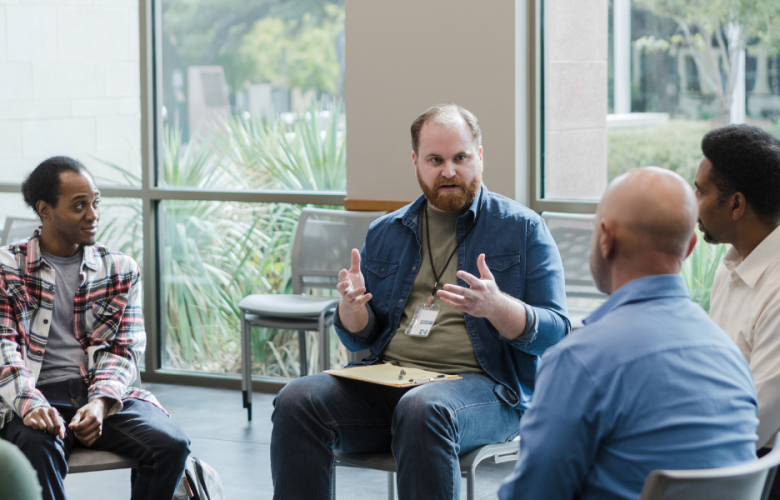 Men sitting on chairs around a circle in a group setting, having a discussion
