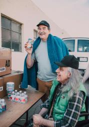 One adult in a wheelchair and one adult holding a cup waiting for food at a food bank.